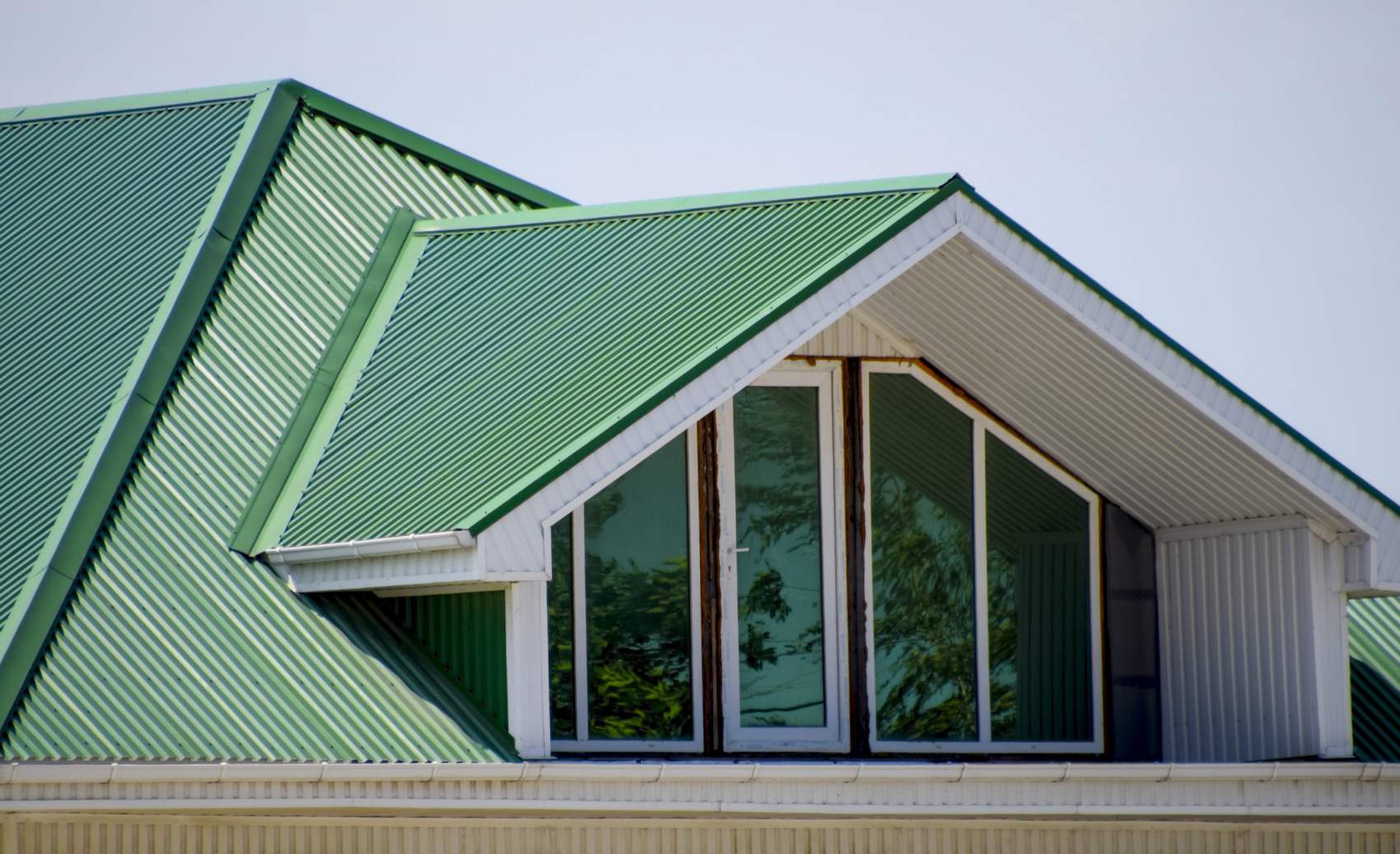 The house with plastic windows and a green roof of corrugated sheet. Roofing of metal profile wavy shape on the house with plastic windows. Green roof of corrugated metal profile and plastic windows.