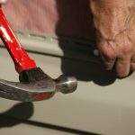 A pair if hands hammering a nail into vinyl siding
