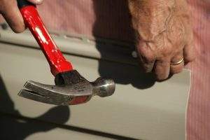 A pair if hands hammering a nail into vinyl siding