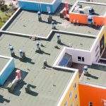 Top view flat roof with air conditioners and hydro insulation membranes on top of a modern blue and orange apartment building sunny summer day.