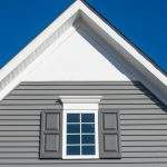 Gable with grey horizontal vinyl lap siding, double hung window with white frame, vinyl shutters on a pitched roof attic at a luxury American single family home neighborhood USA