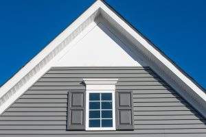 Gable with grey horizontal vinyl lap siding, double hung window with white frame, vinyl shutters on a pitched roof attic at a luxury American single family home neighborhood USA