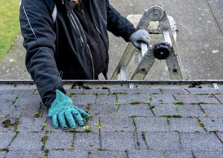 Man inspecting and cleaning dirty moss-covered roof